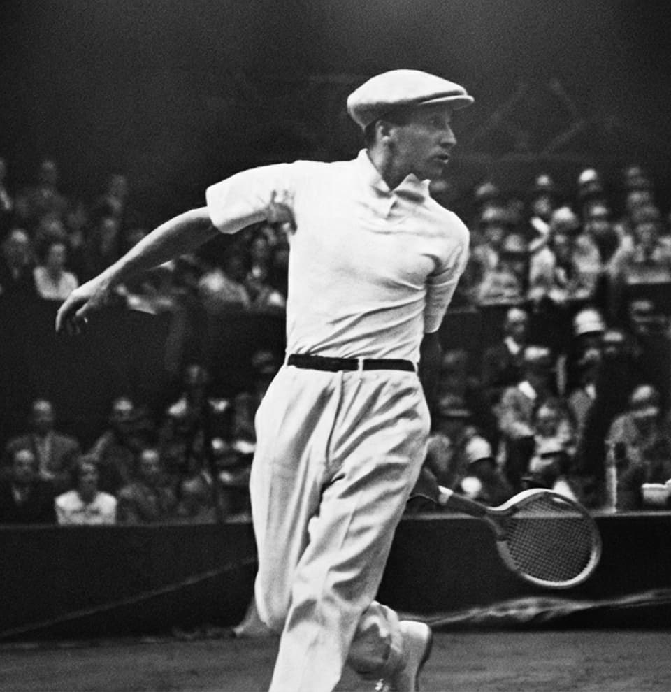 René Lacoste en plena volea en los años 20, con gorra, camisa y pantalón blancos